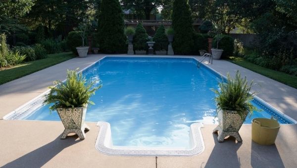 rectangular fiberglass pool with cement patio surrounded by landscaping