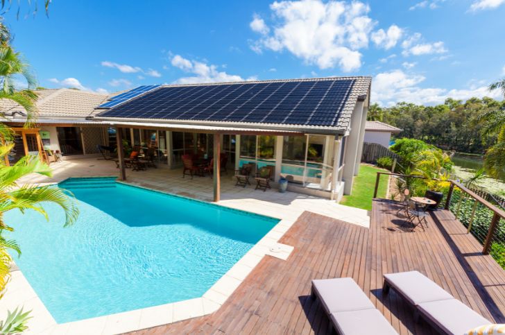 Fiberglass pool with patio and solar panels on roof of house next to pool